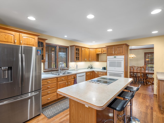 kitchen featuring a kitchen breakfast bar, white appliances, sink, light hardwood / wood-style flooring, and a kitchen island