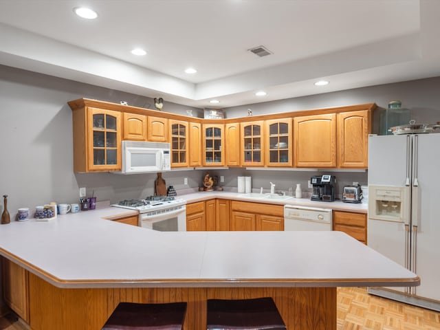 kitchen featuring kitchen peninsula, white appliances, light parquet floors, and a breakfast bar