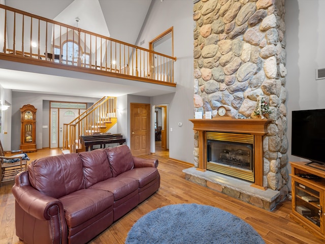 living room featuring hardwood / wood-style floors, high vaulted ceiling, and a stone fireplace