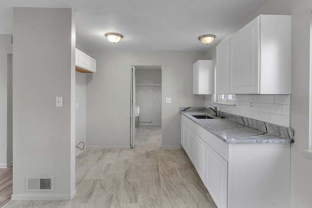 kitchen featuring white cabinets, decorative backsplash, light stone countertops, and sink