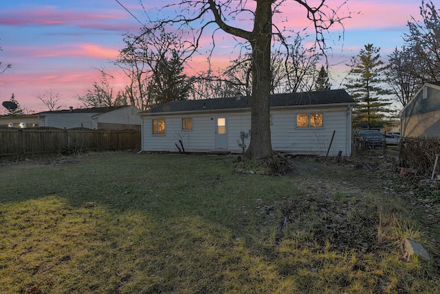 back house at dusk featuring a lawn