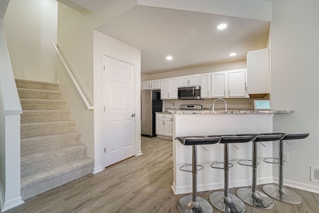 kitchen featuring light stone counters, light wood-type flooring, kitchen peninsula, stainless steel appliances, and white cabinets