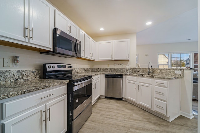 kitchen with appliances with stainless steel finishes, kitchen peninsula, stone countertops, and white cabinets