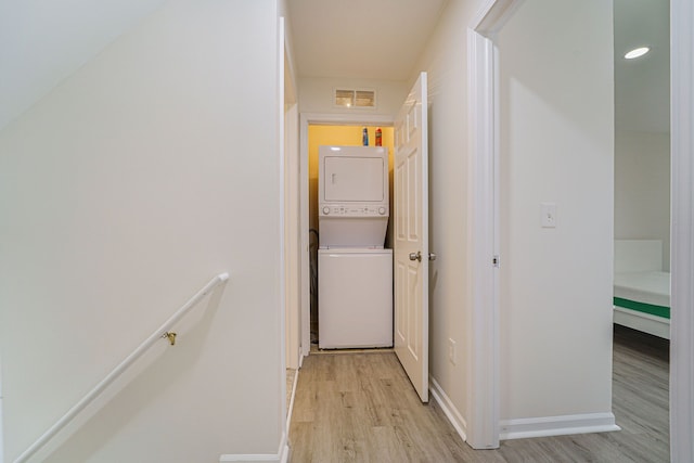 hallway featuring stacked washer and clothes dryer and light hardwood / wood-style floors