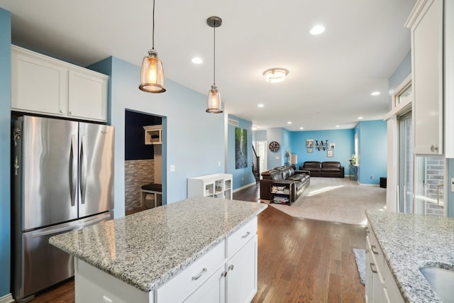 kitchen featuring decorative light fixtures, stainless steel refrigerator, white cabinets, and a kitchen island