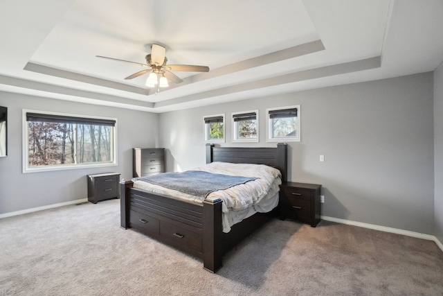 carpeted bedroom featuring multiple windows, a tray ceiling, and ceiling fan