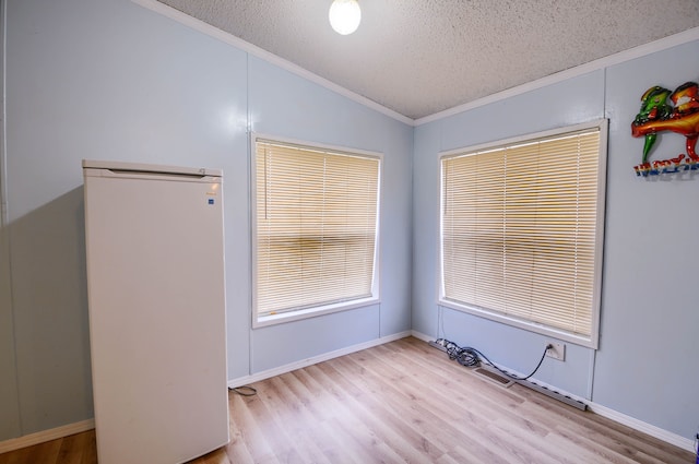 spare room with crown molding, light wood-type flooring, lofted ceiling, and a textured ceiling