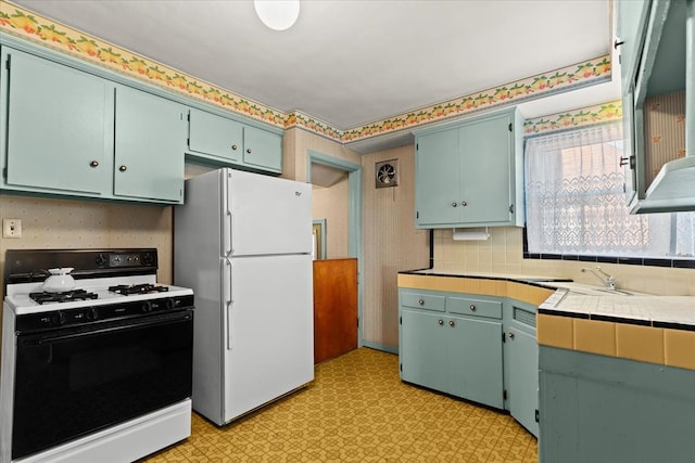 kitchen with gas range, tile counters, white fridge, backsplash, and sink