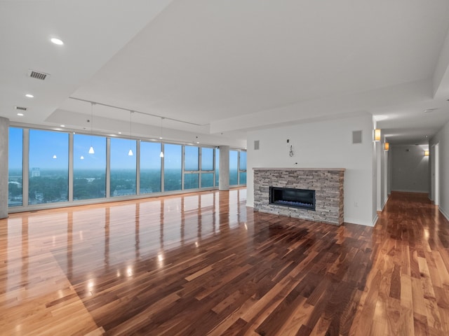 unfurnished living room with hardwood / wood-style flooring, expansive windows, a stone fireplace, and a water view