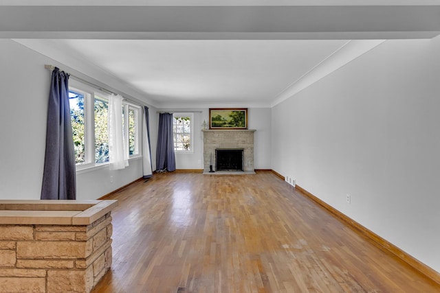 unfurnished living room with a stone fireplace, wood-type flooring, and ornamental molding