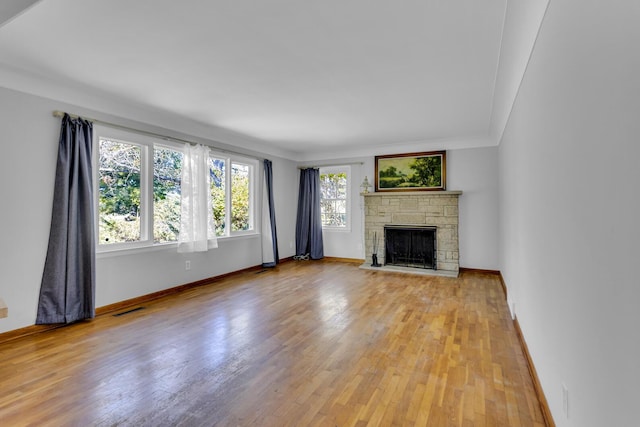 unfurnished living room with light wood-type flooring, a stone fireplace, and ornamental molding