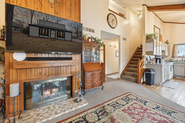 carpeted living room with a fireplace, beam ceiling, and a high ceiling