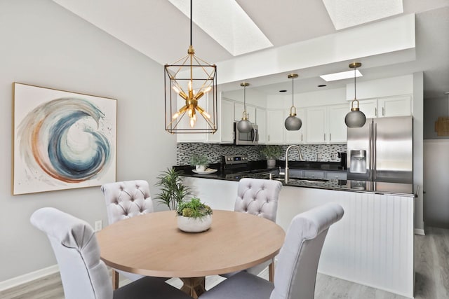 dining room featuring vaulted ceiling with skylight, light wood-type flooring, sink, and a chandelier