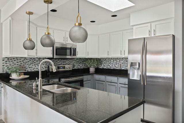 kitchen featuring white cabinets, dark stone countertops, stainless steel appliances, and a skylight