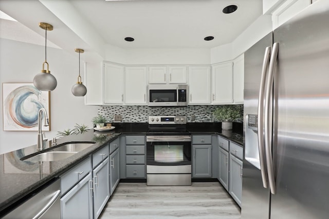 kitchen with appliances with stainless steel finishes, light wood-type flooring, sink, decorative light fixtures, and white cabinets