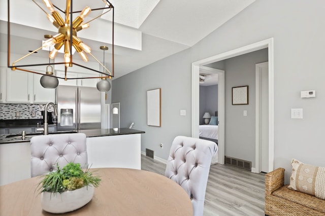 dining room featuring sink, a chandelier, vaulted ceiling, and light wood-type flooring