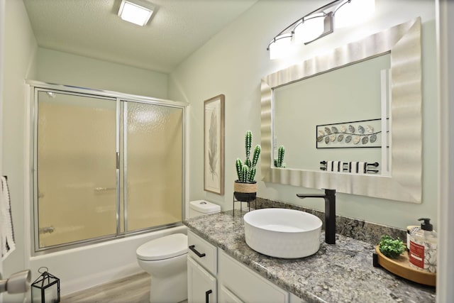 full bathroom featuring bath / shower combo with glass door, vanity, a textured ceiling, hardwood / wood-style flooring, and toilet