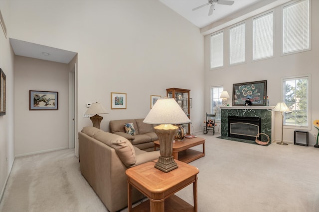 living room featuring light carpet, a high ceiling, ceiling fan, and a premium fireplace