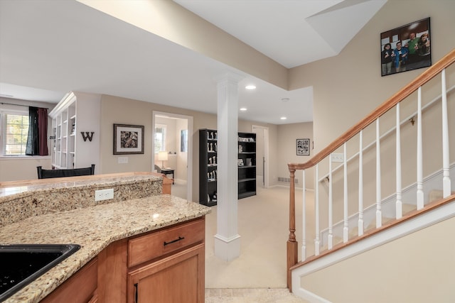 kitchen featuring light stone countertops, light colored carpet, ornate columns, and sink