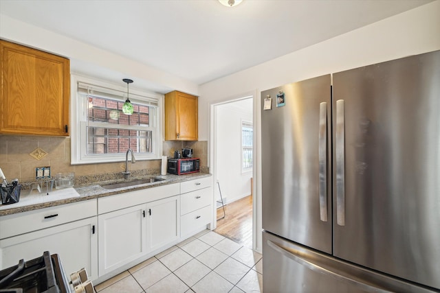 kitchen featuring stainless steel refrigerator, sink, light tile patterned floors, light stone counters, and white cabinets