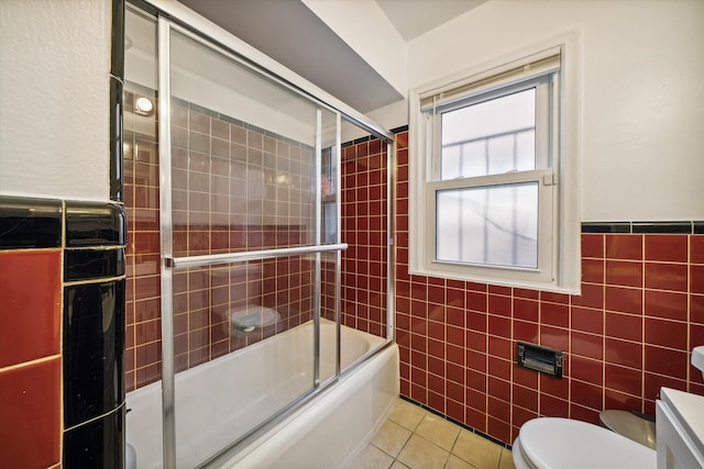 bathroom with combined bath / shower with glass door, tile patterned floors, tile walls, and toilet