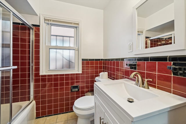 full bathroom with tile patterned floors, combined bath / shower with glass door, toilet, vanity, and tile walls