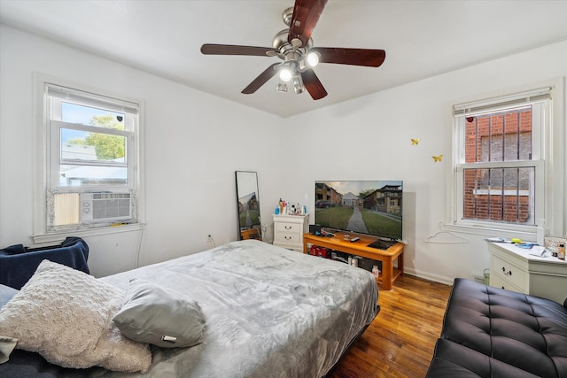 bedroom with ceiling fan, cooling unit, wood-type flooring, and multiple windows