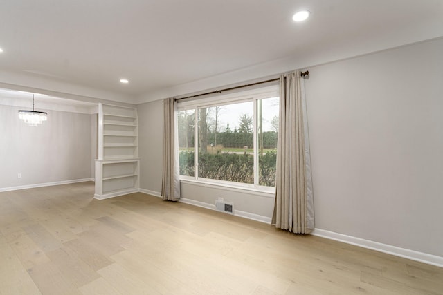 spare room with a chandelier and light wood-type flooring