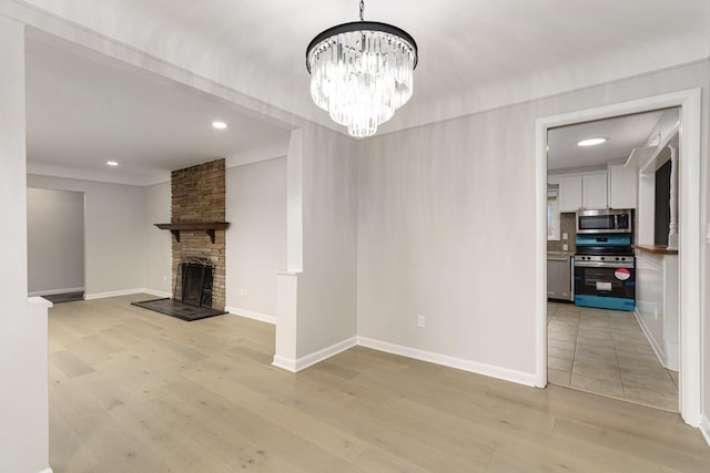 unfurnished living room featuring a stone fireplace, light hardwood / wood-style floors, and a notable chandelier