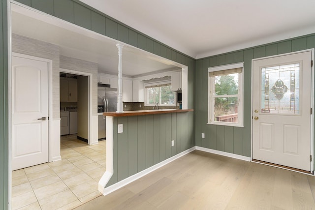 kitchen featuring white cabinetry, stainless steel refrigerator with ice dispenser, light hardwood / wood-style floors, separate washer and dryer, and kitchen peninsula