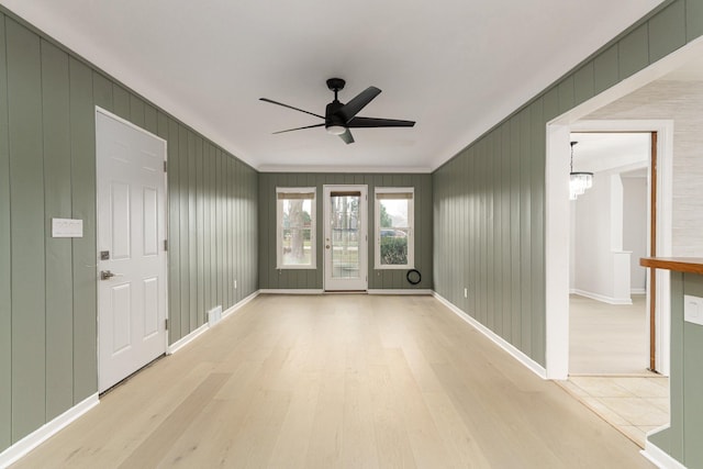 spare room with ceiling fan with notable chandelier, ornamental molding, wood walls, and light wood-type flooring