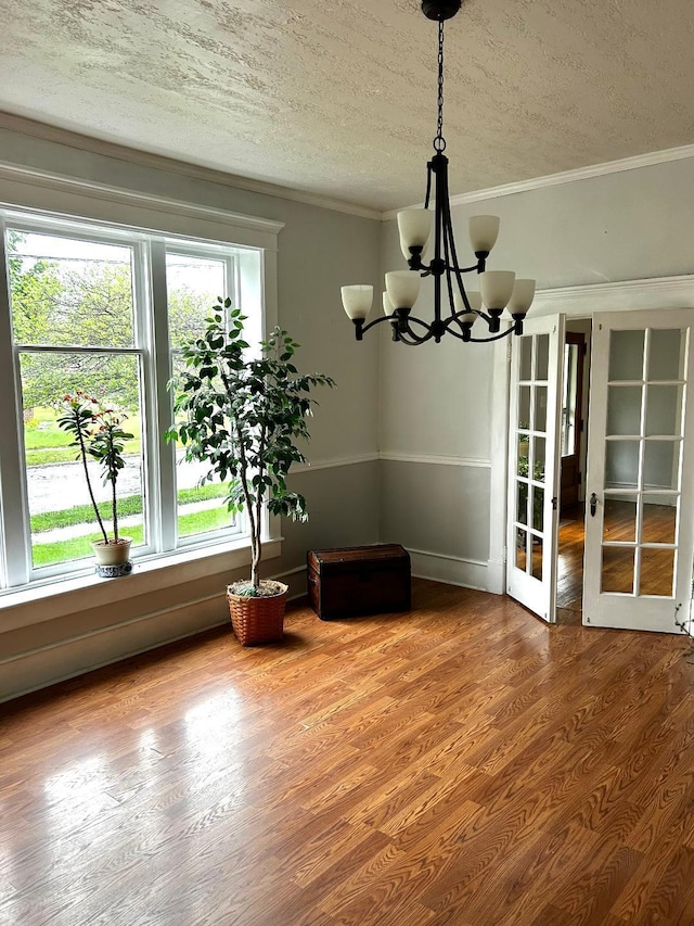 dining area with french doors, wood finished floors, a textured ceiling, ornamental molding, and an inviting chandelier