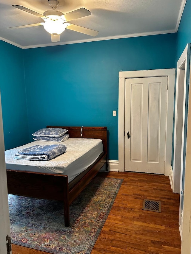 bedroom featuring baseboards, ceiling fan, visible vents, crown molding, and wood finished floors