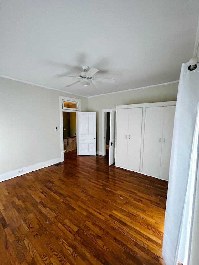 unfurnished bedroom featuring ornamental molding, two closets, ceiling fan, dark wood-style floors, and baseboards