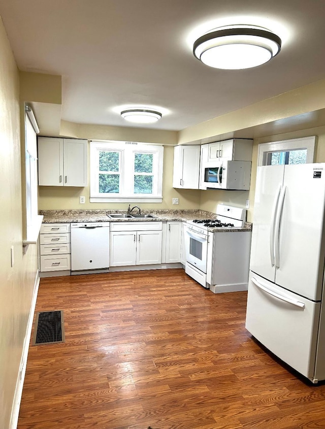 kitchen featuring dark wood-style flooring, white appliances, visible vents, a sink, and white cabinets