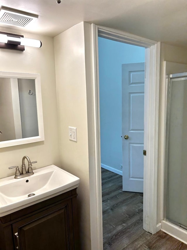 bathroom with wood finished floors, vanity, visible vents, a shower stall, and baseboards