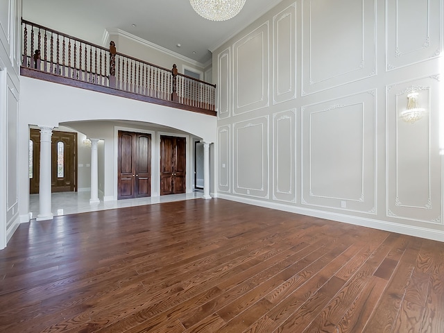 unfurnished living room featuring a high ceiling, decorative columns, dark hardwood / wood-style floors, and ornamental molding