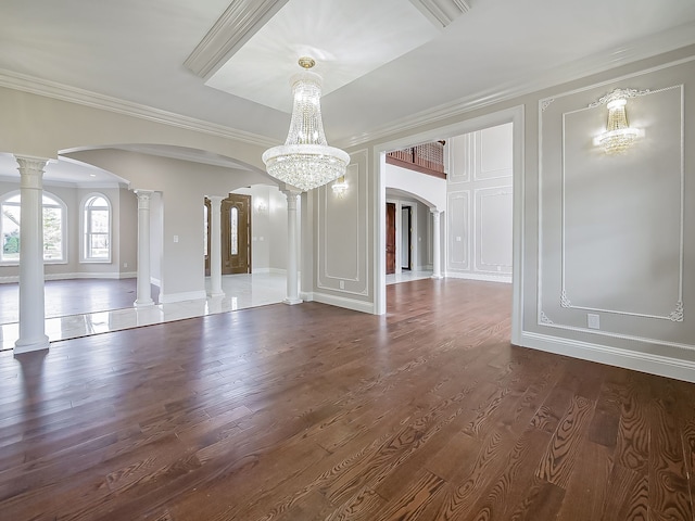 unfurnished dining area featuring ornate columns, crown molding, dark wood-type flooring, and an inviting chandelier