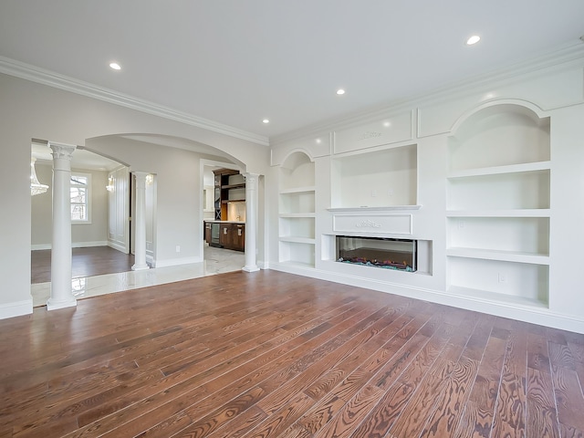 unfurnished living room featuring built in shelves, ornate columns, ornamental molding, and wood-type flooring