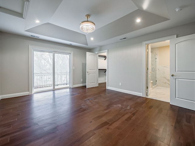 unfurnished bedroom featuring access to exterior, dark hardwood / wood-style flooring, a raised ceiling, and connected bathroom