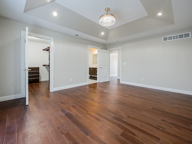 unfurnished bedroom with a tray ceiling, a walk in closet, dark hardwood / wood-style flooring, and ensuite bath