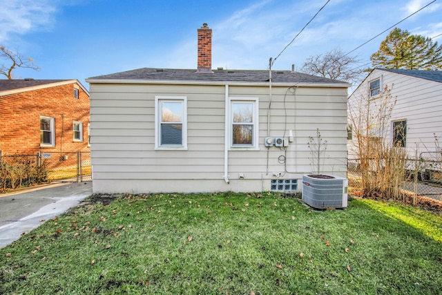 rear view of house with central AC unit and a lawn