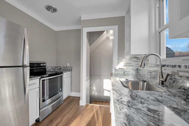 kitchen with white cabinetry, sink, light stone countertops, hardwood / wood-style floors, and appliances with stainless steel finishes