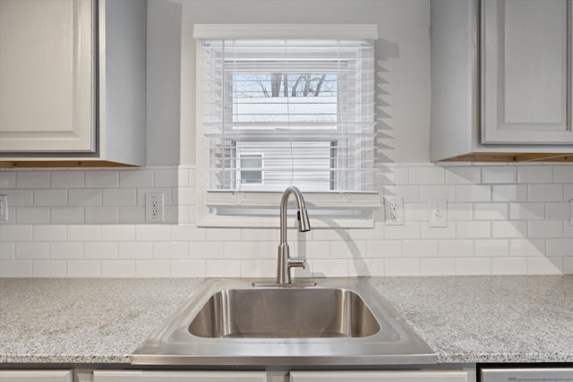 kitchen featuring decorative backsplash, light stone counters, and sink