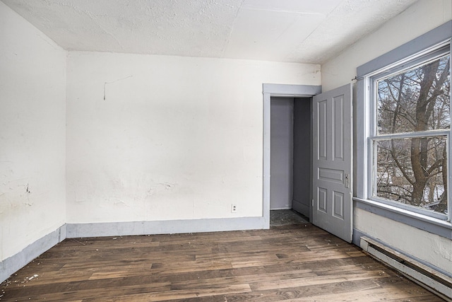 empty room with a textured ceiling, dark hardwood / wood-style flooring, and baseboard heating