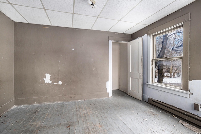 unfurnished room featuring hardwood / wood-style floors, a baseboard radiator, and a drop ceiling