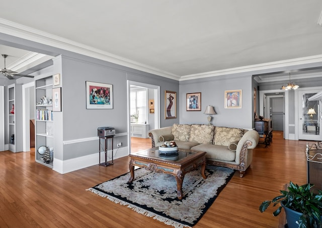 living area featuring baseboards, ornamental molding, wood finished floors, and ceiling fan with notable chandelier