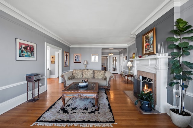 living area with baseboards, a fireplace, ornamental molding, and wood finished floors