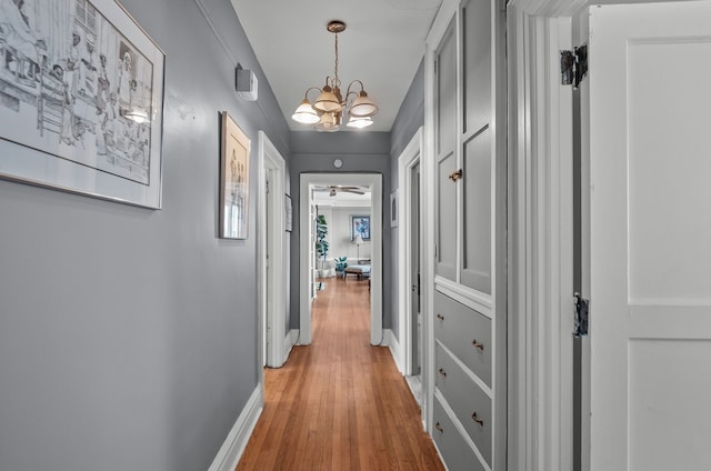 hall with baseboards, light wood finished floors, and an inviting chandelier