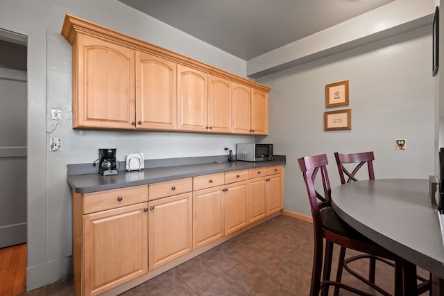 kitchen with dark countertops, stainless steel microwave, baseboards, and light brown cabinetry